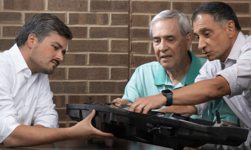 Three problem solvers discussing and examining an automotive cover