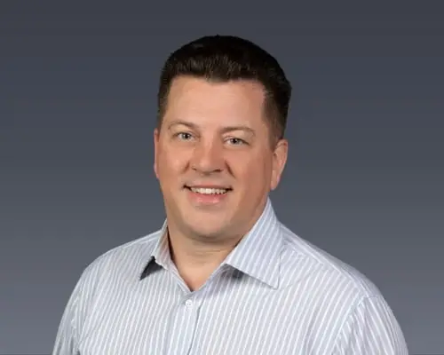 Headshot of Tom Smith in front of a charcoal grey background.