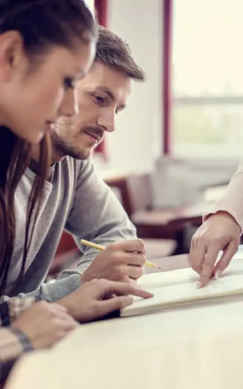 Man and Woman sitting side-by-side at a table reviewing notebook